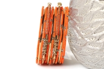 Bright colored elegant looking gold colored metal fashion bangles set of 12 pieces has small orange beads on 7 thin bangles, 3 thin gold colored bangles & 2 are resin bangles encrusted in patterned gold colored metal frame.